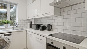 A modern kitchen with white cabinetry, a built-in dishwasher, a stovetop, and a window with a view of industrial structures. - NEW LISTING!!! South Kensington Style newly refurbished apartment (London)