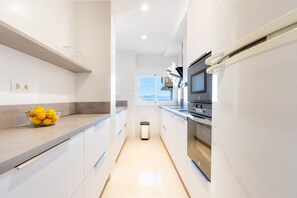 A modern kitchen with white cabinetry, a stainless steel oven, and a bowl of lemons on the counter.