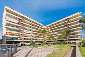 A multi-story hotel with balconies, a central courtyard, and palm trees. - La Carihuela II | Stylish Coastal Apartment with Terrace, Pool & Beach (Torremolinos)