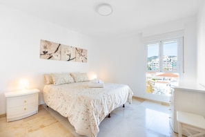 A bedroom with a bed, a nightstand, a desk, and a window with a view of buildings. - La Carihuela II | Stylish Coastal Apartment with Terrace, Pool & Beach (Torremolinos)