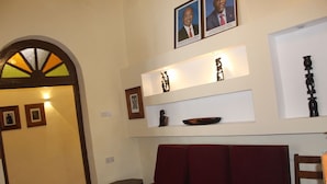 A room with a red sofa, a wooden chair, a small table, and a wall with framed pictures and decorative items. - The Island Stone Town Hotel  (Zanzibar Town)