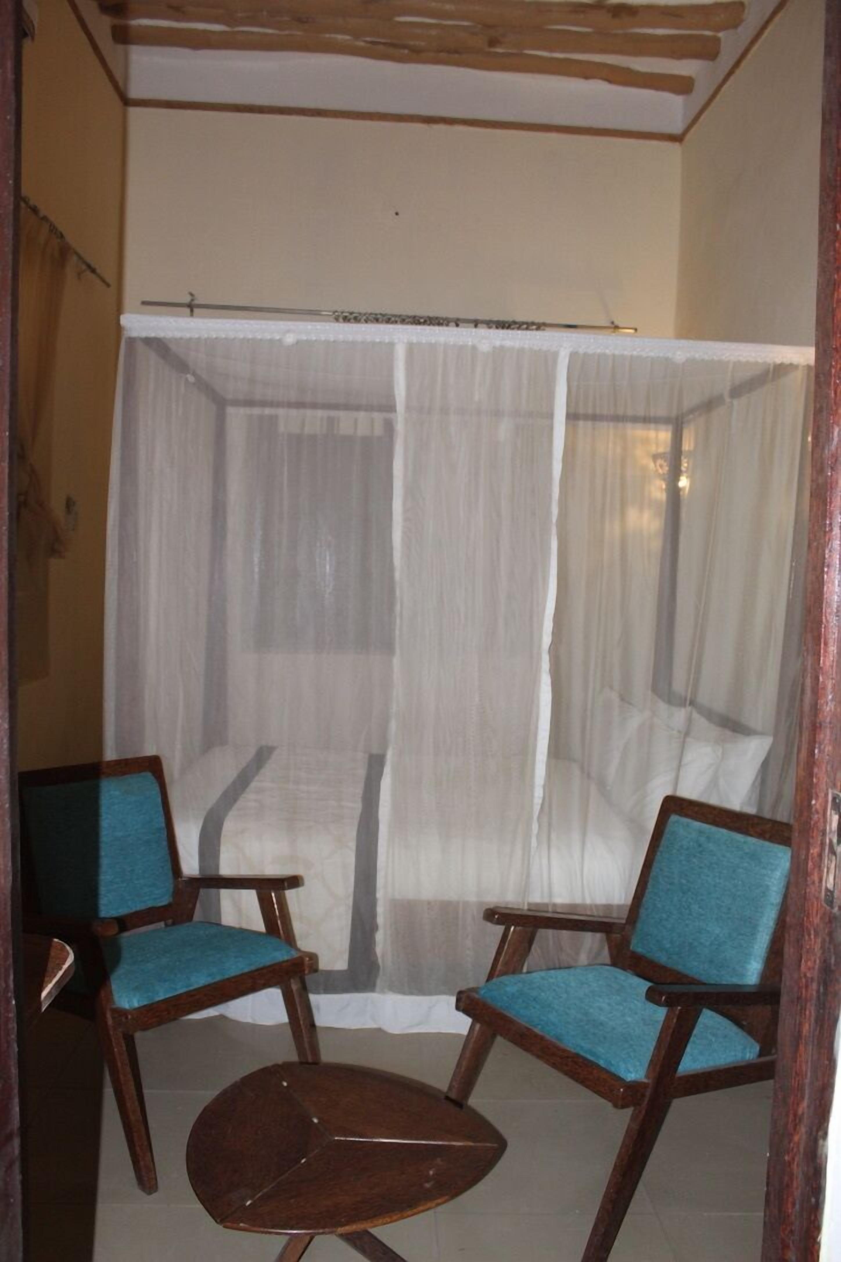 A room with a canopy bed, two chairs, and a small table.