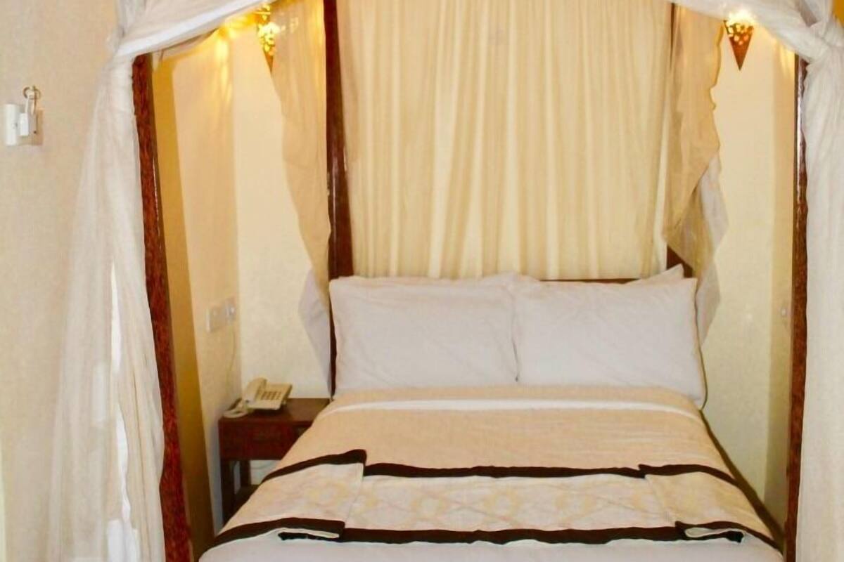 A bed with a canopy, a bedside table with a phone, and a wall-mounted light fixture.