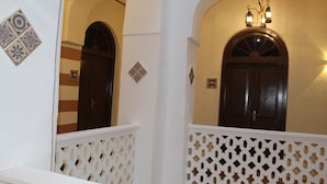 A hallway with a white lattice railing, a wooden door, and a wall with decorative tiles. - The Island Stone Town Hotel  (Zanzibar Town)