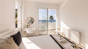 A bedroom with a bed, a desk, a chair, a mirror, a radiator, and a view of the sea. - Faros Beachfront Villa Larnaca (Larnaca)
