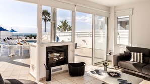 A modern living room with a fireplace, a sofa, and a dining area with a pool view. - Faros Beachfront Villa Larnaca (Larnaca)