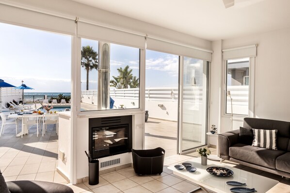A modern living room with a fireplace, a sofa, and a dining area with a pool view.