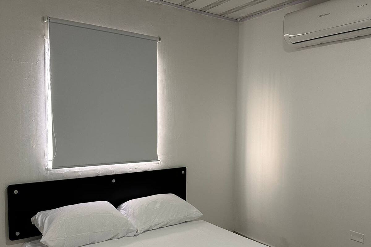 A single bed with white bedding, a black headboard, and a window with blinds.
