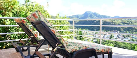 Two lounge chairs with patterned cushions on a balcony with a view of a town and mountains.