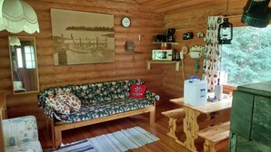 A cozy cabin interior with a wooden sofa, a wooden table, a clock, and a painting of a dock.
