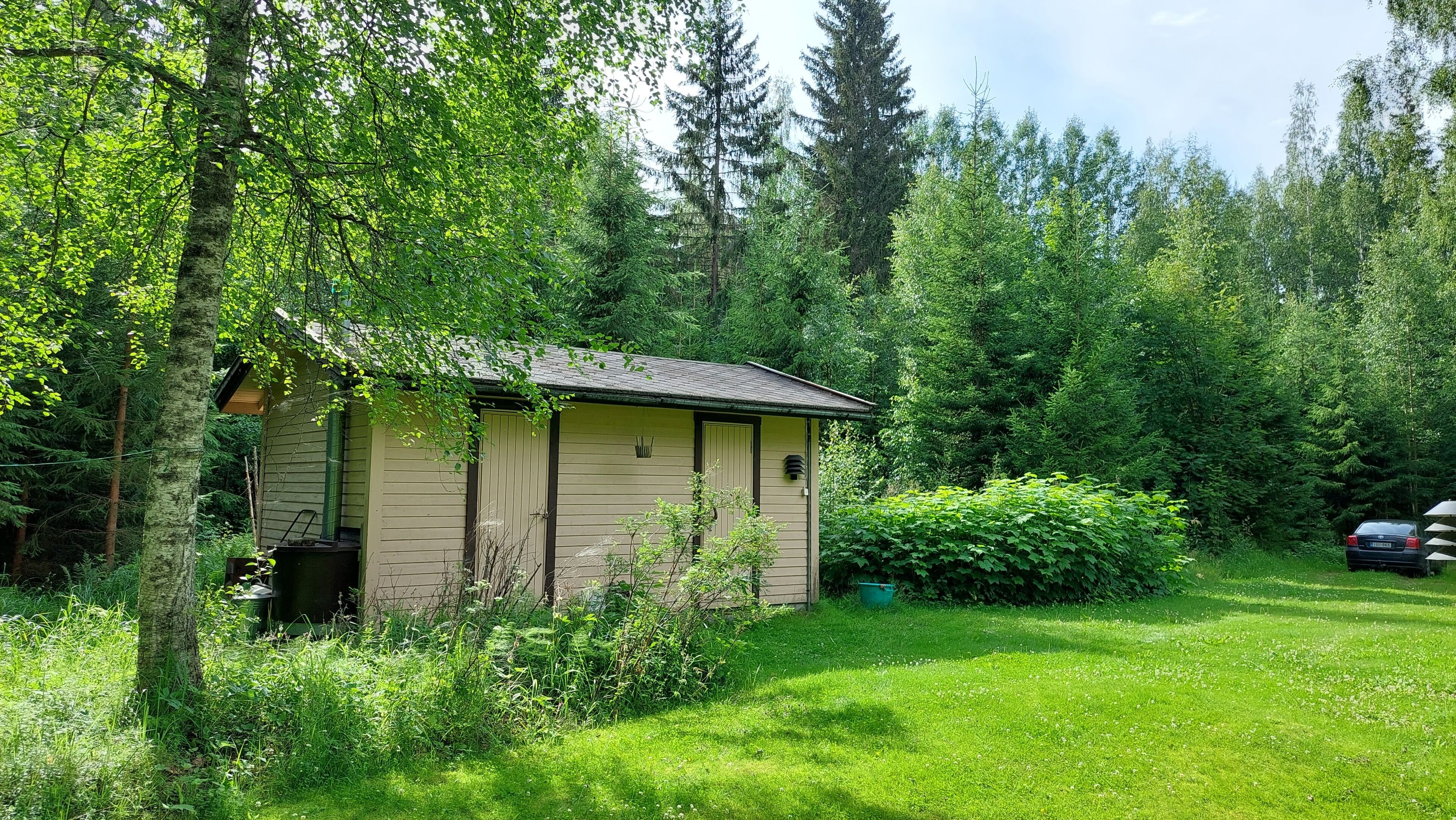 A small, single-story cabin with a sloped roof, surrounded by dense forest.