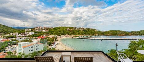 Un balcón con dos sillas y una mesa, con vista a una playa y un pueblo costero.