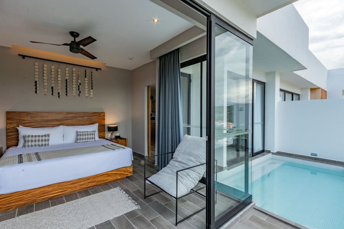 A modern bedroom with a large bed, a ceiling fan, and a glass-enclosed balcony with a pool.