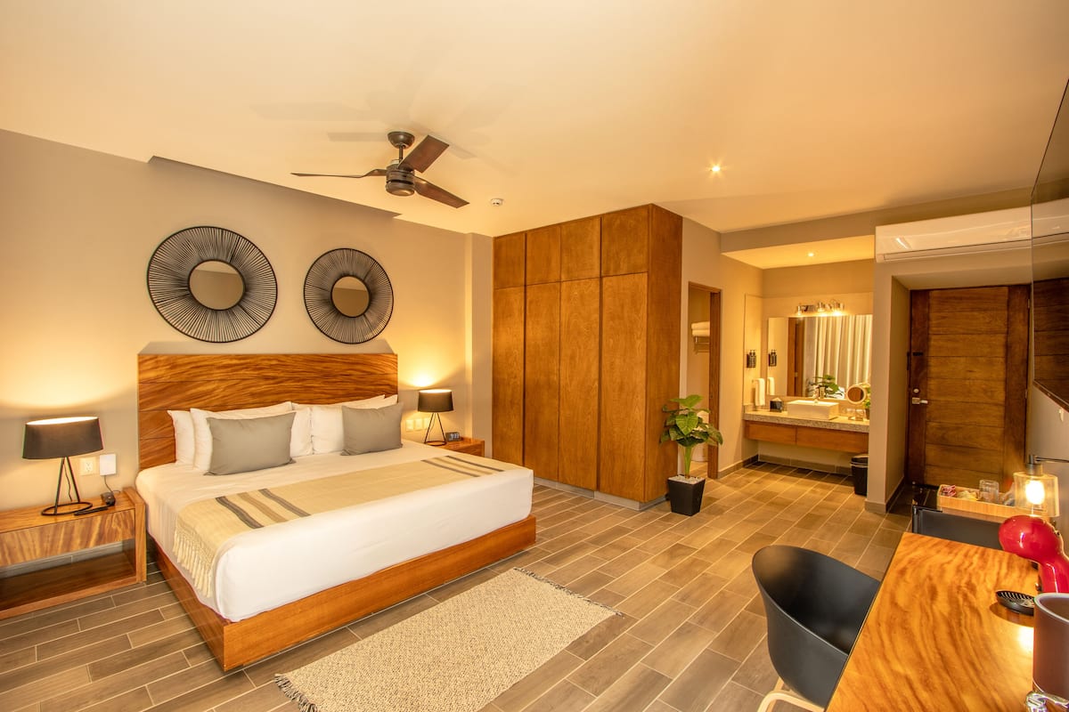 A modern hotel room with a large bed, a desk, a chair, and a bathroom with a mirror and sink.