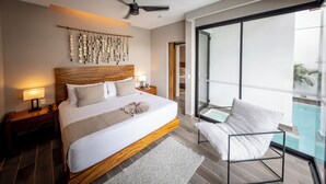 Habitación de hotel moderna con una cama grande, un ventilador de techo, una mesita de noche con lámpara, vistas a una piscina a través de un ventanal y una silla junto a la piscina.