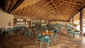 Un amplio comedor interior con suelo de madera y sillas verdes, que cuenta con un tejado de paja y varias mesas.