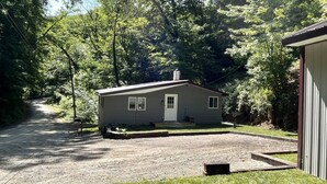 A small, single-story cabin with a gravel driveway and a grassy lawn, surrounded by dense trees. - Nature's Grove Cabin

 (Delta)