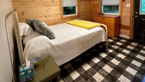 A small, cozy room with a bed, a nightstand, and a dresser. There are two windows with blinds, and the floor has a checkered pattern. - Nature's Grove Cabin

 (Delta)