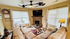 Ein Wohnzimmer mit einem beigen Sofa, einem Kamin aus Stein, einem Deckenventilator und einem Fernseher.