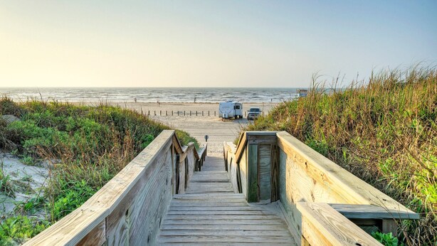 A wooden boardwalk leading to a beach with a dune and a dune buggy parked at the end. - Holiday Beach House by Avantstay Pool + Beach (Port Aransas)