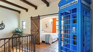 A bedroom with a bed, a blue telephone booth, and a wooden door. - Luxe 7bdr Oasis w/ Pool, Putting Green, Game Room Villa Del Gallo by Avantstay (Indio)