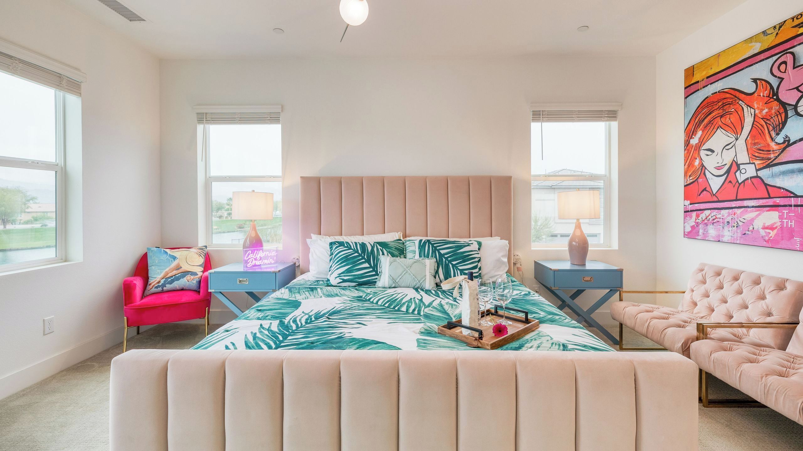 A bedroom with a bed, two nightstands, a chair, a couch, and a large window.