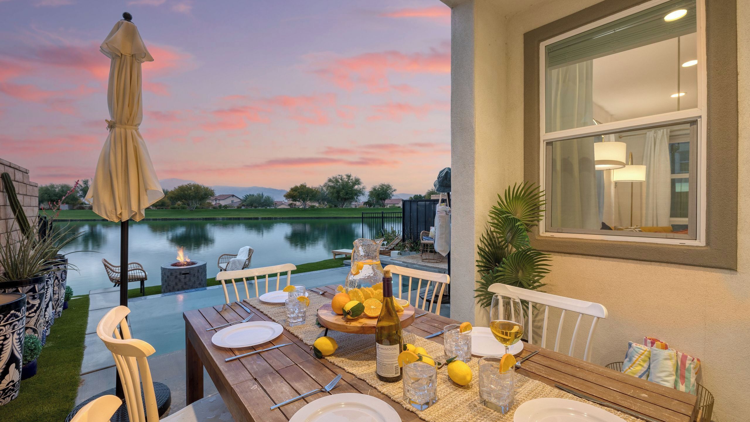 Une table à manger installée à l’extérieur, avec vue sur un lac et le coucher de soleil.