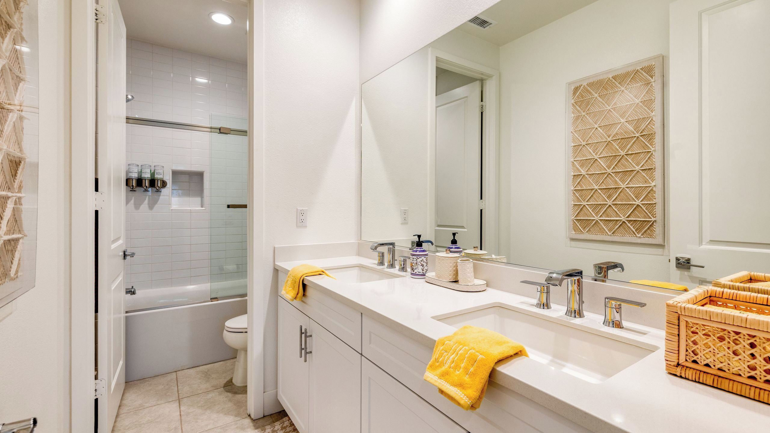 Een moderne badkamer met douche, toilet en twee wasbakken met een grote spiegel.