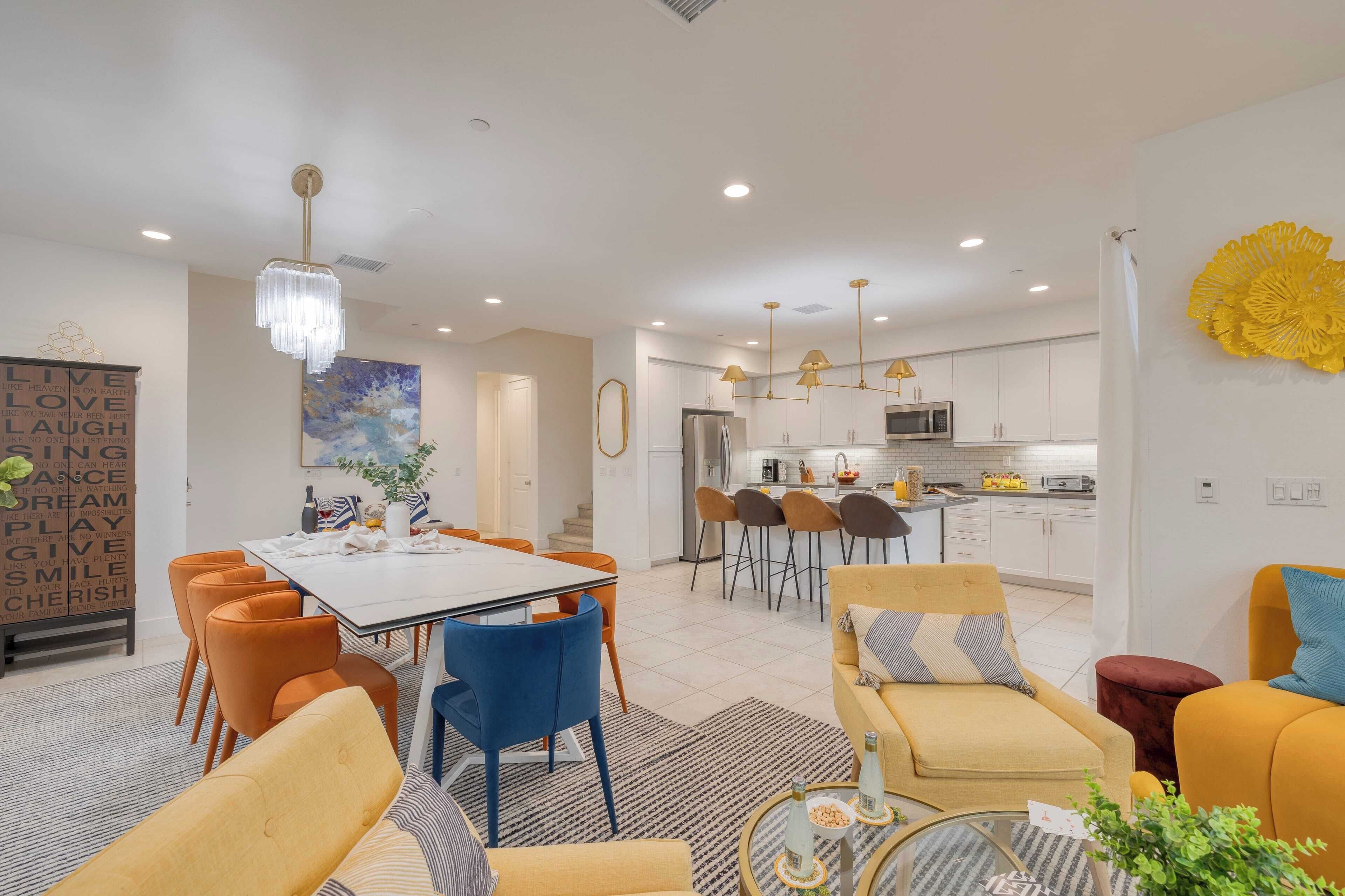 A modern living room with a dining area, kitchen, and a large yellow decorative piece on the wall.
