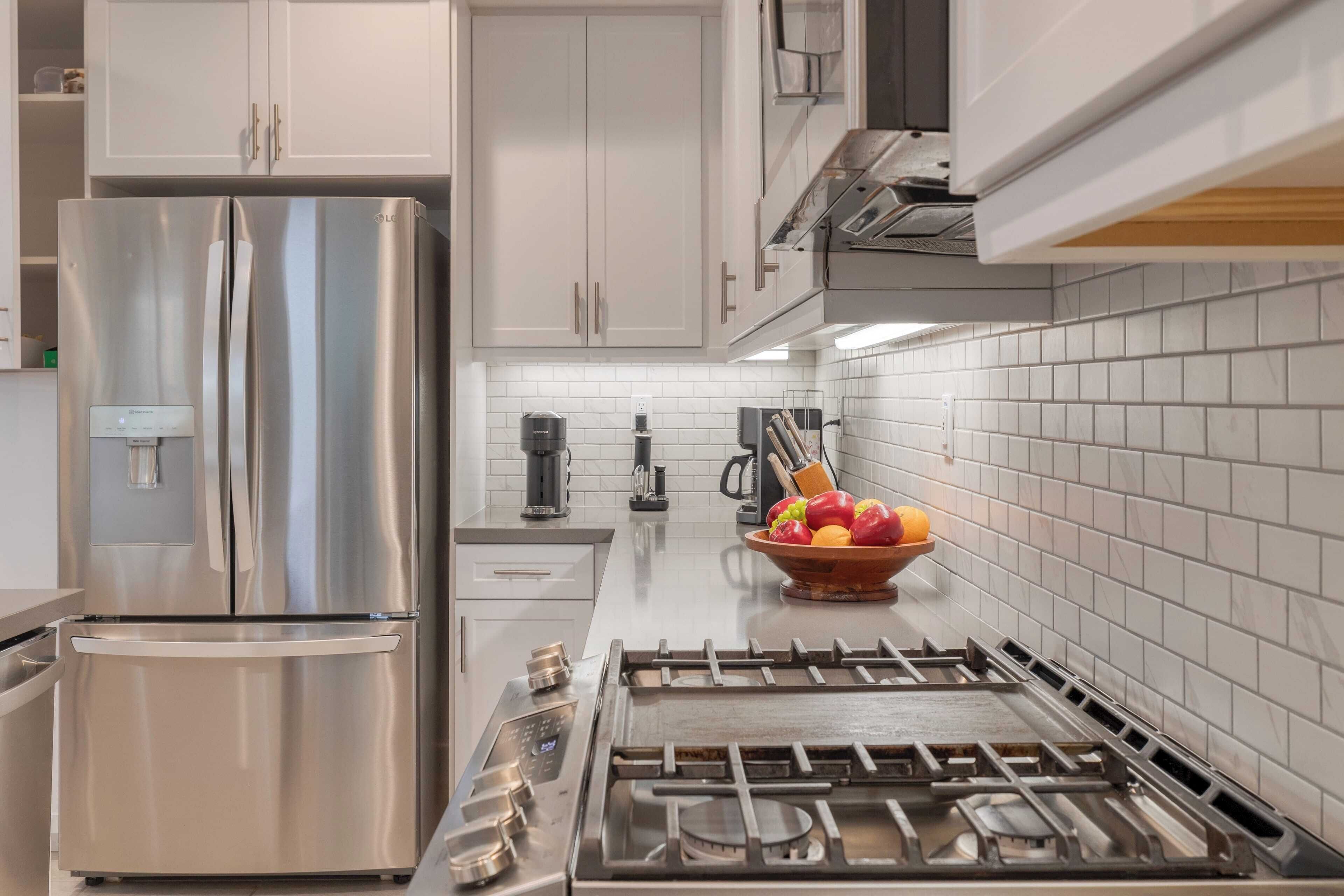 A modern kitchen with stainless steel appliances, white cabinets, and a tiled backsplash.