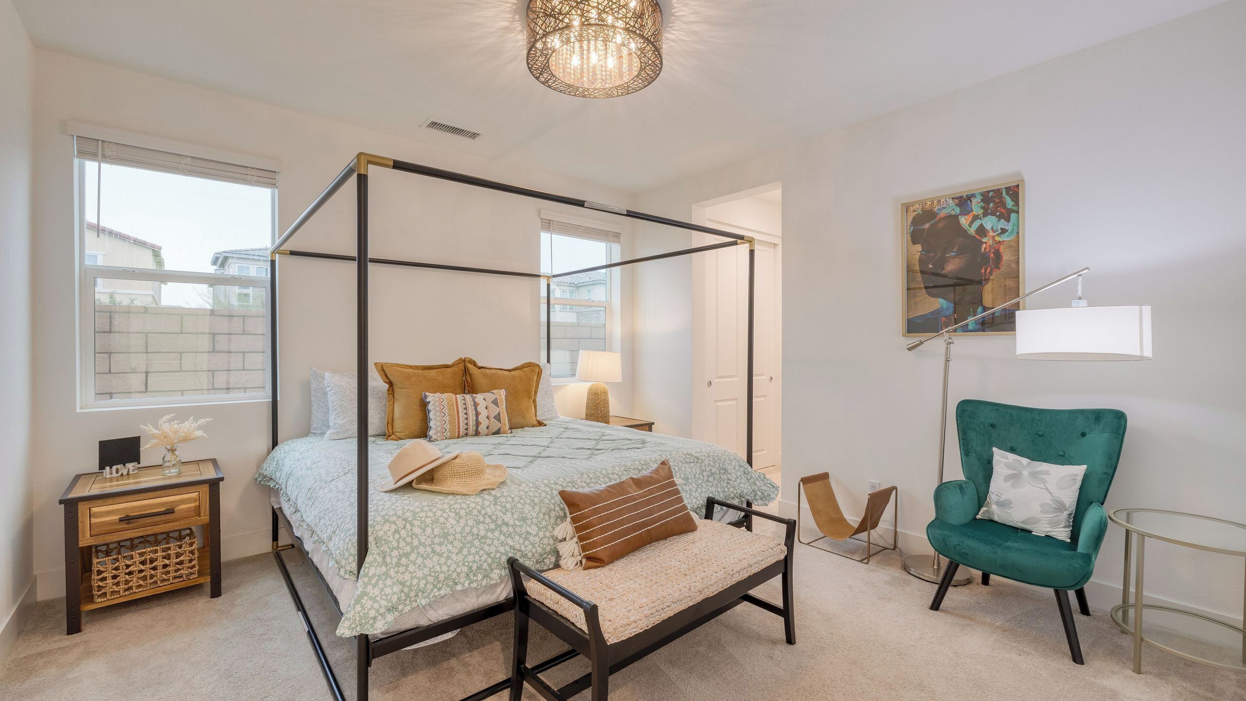 A four-poster bed with a canopy, a green armchair, a small table, and a painting on the wall.