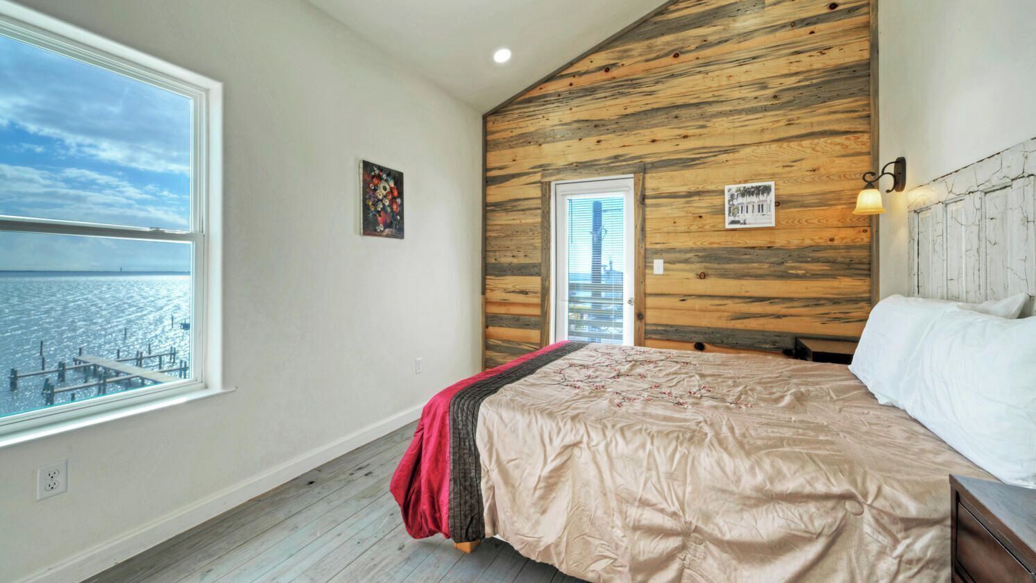 Une chambre avec une grande fenêtre, un lambris en bois, un lit recouvert d’une couverture rouge et une vue sur le paysage urbain.