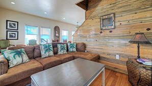 A living room with a wooden wall, a brown leather sofa, and a metal coffee table. - Waterfront w/ Bay Views, Shared Pool & Boat Dock Marlin Madness by Avantstay (Corpus Christi)