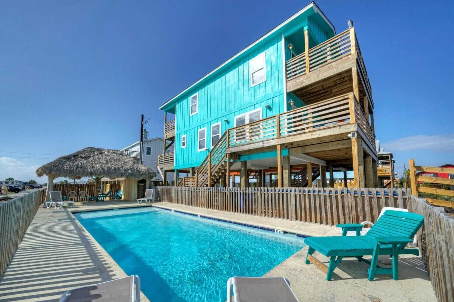 A turquoise two-story building with a wooden deck and a swimming pool.