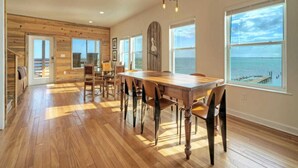 A spacious dining area with a large wooden table and chairs, large windows with ocean views, and a rustic wooden interior. - Waterfront w/ Bay Views, Shared Pool & Boat Dock Marlin Madness by Avantstay (Corpus Christi)