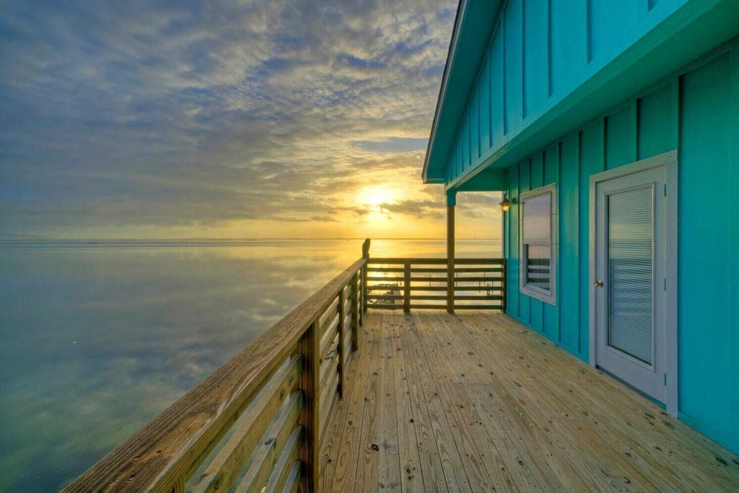A wooden deck with a view of the ocean and a sunset.