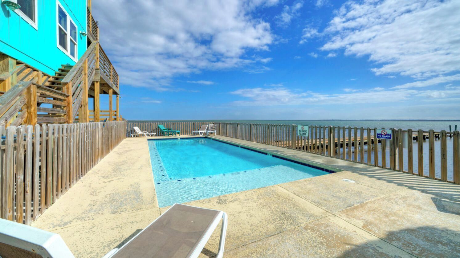 Un espace piscine doté d’une terrasse en bois, de chaises longues et offrant une vue sur l’océan.