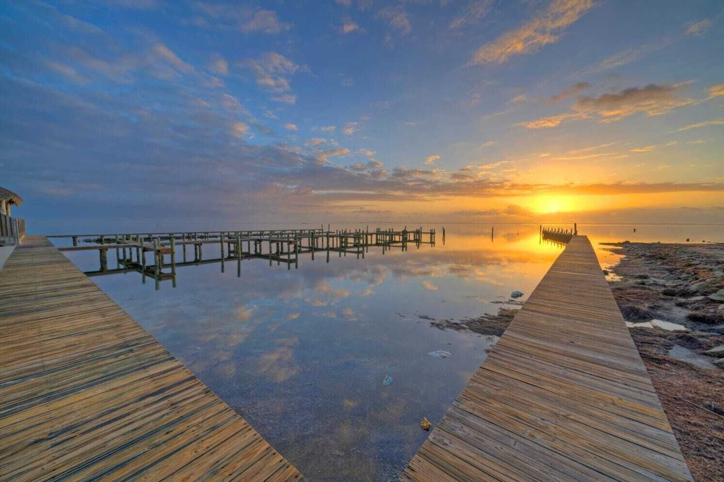 A wooden pier extending into calm waters at sunset, with a clear sky above.