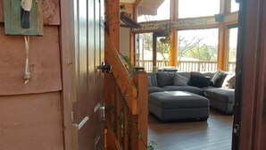 Una porta in legno che dà su un soggiorno con un divano grigio, una scala e un lampadario.