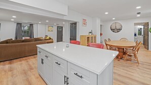 Una cucina moderna con mobili bianchi, un'isola centrale e una zona pranzo con tavolo e sedie in legno.