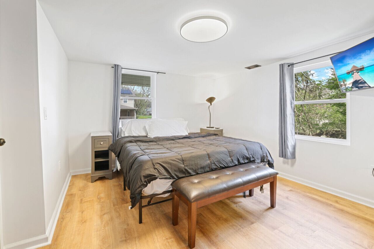 Een slaapkamer met een bed, een bankje, een nachtkastje, een lamp en een raam met uitzicht op het landschap.