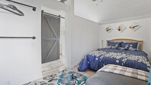 A bedroom with a bed, a ceiling fan, a wooden door, and a wall-mounted rack.