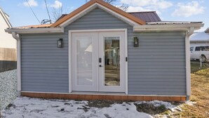 A small, single-story building with a gray exterior, a white front door, and a brown roof.