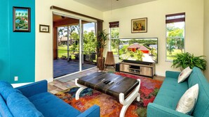 Ein Wohnzimmer mit großem Fernseher, blauen Sofas, einem Couchtisch und einem Deckenventilator.