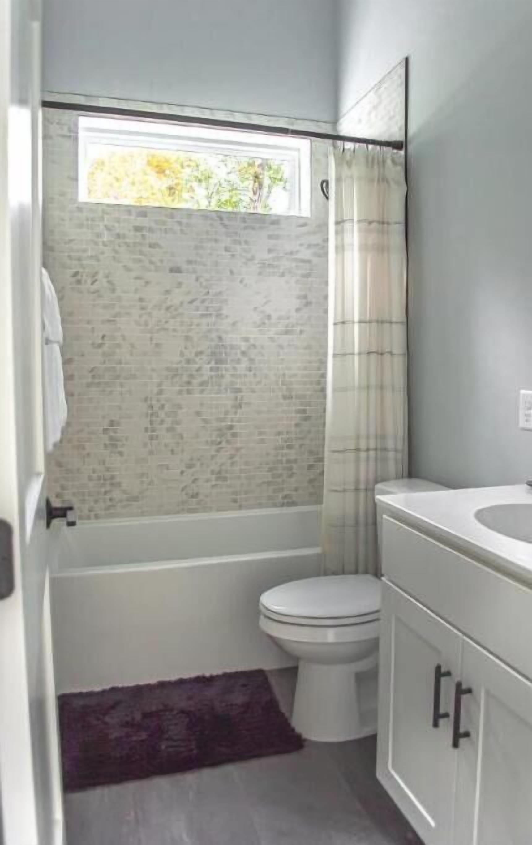 A bathroom with a toilet, a sink, and a window above the shower.