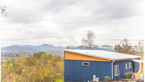 Un bâtiment d’un seul étage, doté d’un toit en pente, entouré d’arbres et avec des montagnes en arrière-plan.