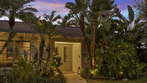 A house with a front door, surrounded by tropical plants and a pathway leading to the entrance.