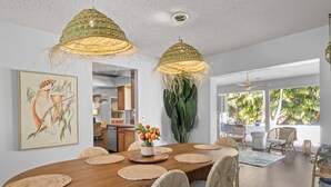A spacious dining area with a wooden table, woven chairs, and a large painting on the wall.