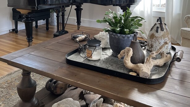 Een vleugelpiano in een goed verlichte kamer met een houten vloer, een dienblad met decoratieve objecten en uitzicht op het buitenlands landschap door grote ramen.