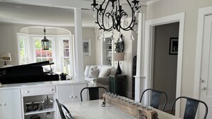 Een eetruimte met een lange houten tafel, stoelen, een kroonluchter en een piano.